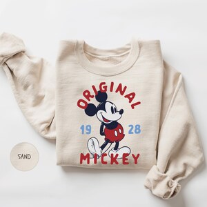 A beige sweater with a graphic of Mickey Mouse and text that reads "ORIGINAL" and "1928" printed on it.
