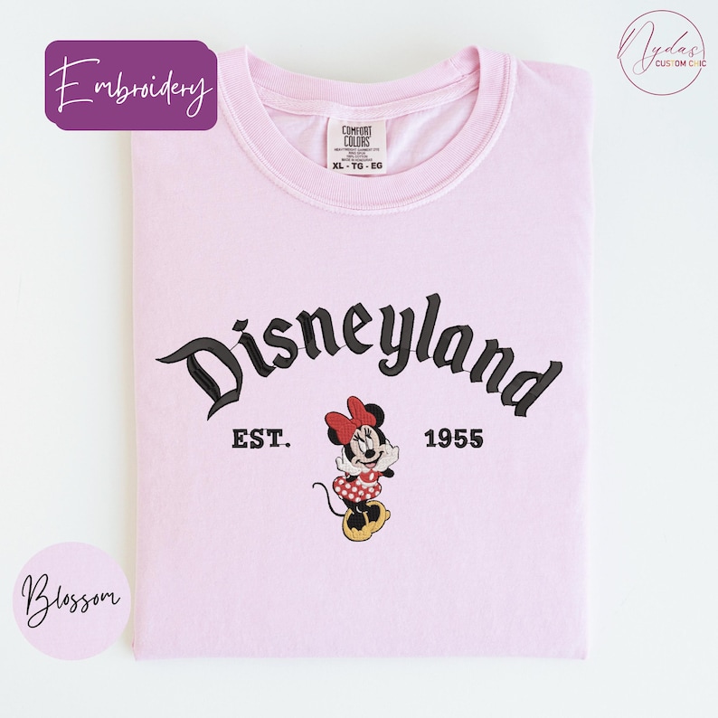 A pink t-shirt with the text "Disneyland EST. 1955" and a Minnie Mouse graphic, indicating the establishment year of the theme park.