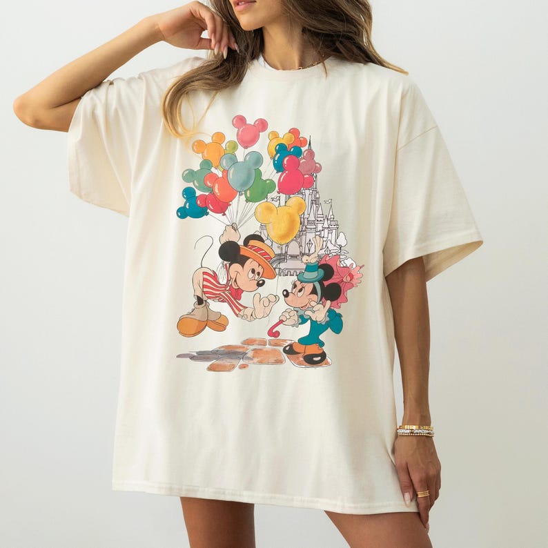 A woman wearing a white t-shirt with a colorful graphic of Mickey Mouse and Minnie Mouse surrounded by balloons.