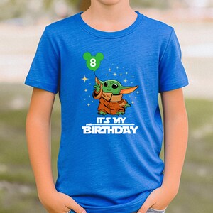 A blue t-shirt with a graphic of a young child holding a green balloon and the text "It's my birthday" printed on it.