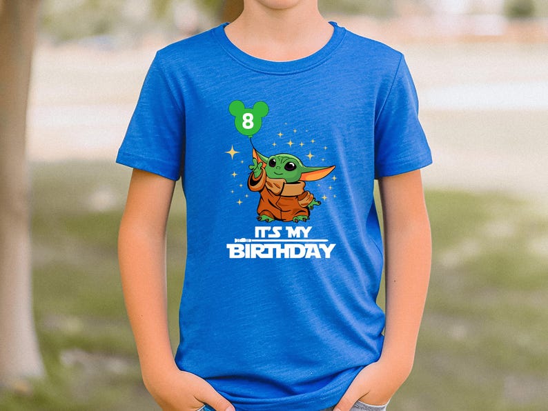 A blue t-shirt with a graphic of a young child holding a green balloon and the text "It's my birthday" printed on it.
