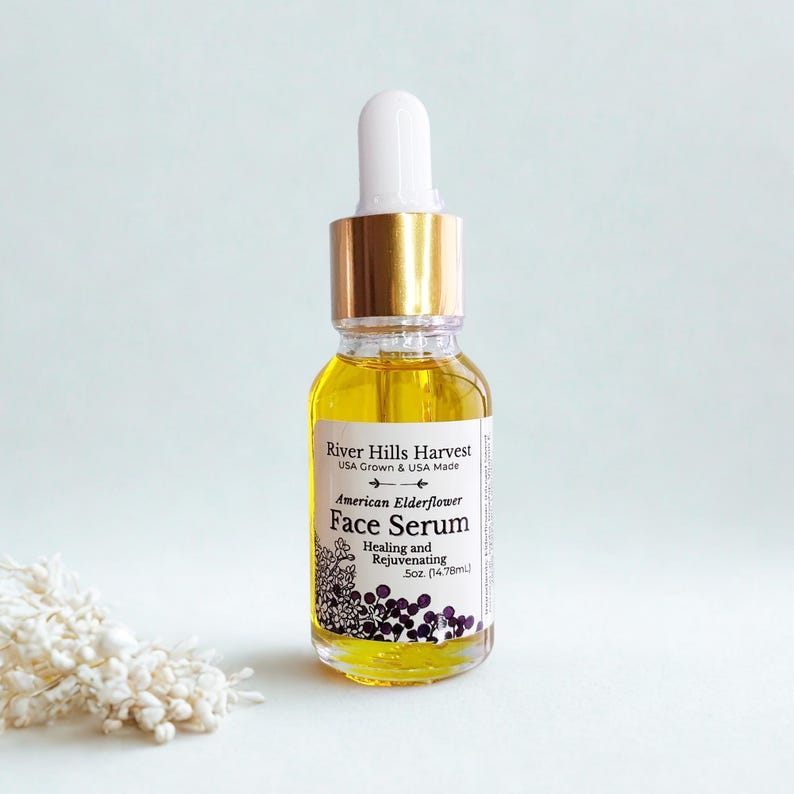 May include: A clear glass bottle of River Hills Harvest American Elderflower Face Serum. The bottle has a gold cap and white dropper. The label includes text: "Healing and Rejuvenating" and "5oz. (14.78ml)".