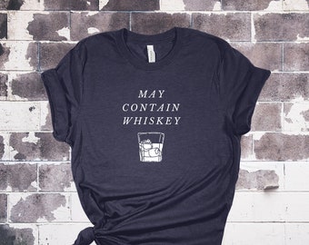 Puede incluir: Una camiseta azul oscuro con el texto "MAY CONTAIN WHISKEY" y un dibujo de un vaso de whisky con cubitos de hielo.