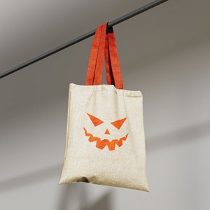 May include: A beige tote bag with orange straps and a jack-o'-lantern face printed on the front.