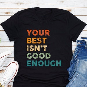 May include: Black t-shirt with a vintage-style graphic that reads "YOUR BEST ISN'T GOOD ENOUGH" in rainbow colours.