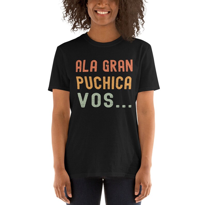 May include: A black t-shirt with a vintage-style graphic that reads "ALA GRAN PUCHICA VOS..." in orange, yellow, and green.