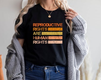 May include: A black t-shirt with the text "Reproductive Rights Are Human Rights" in a vintage style font with orange, yellow, and brown stripes.