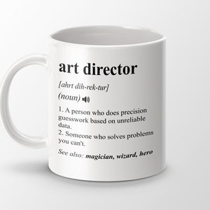Könnte beinhalten: Weiße Keramiktasse mit einem schwarzen Design, das den Begriff "Art Director" mit einer humorvollen Definition definiert. Die Tasse hat einen schwarzen Henkel.