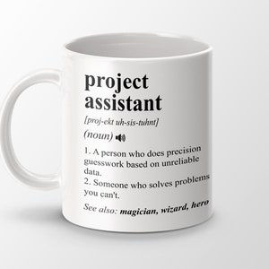 Op de afbeelding: Witte keramische mok met een zwart ontwerp dat het woord "projectassistent" en de uitspraak ervan definieert. De definitie omvat twee opsommingspunten en de zin "Zie ook: tovenaar, tovenaar, held".
