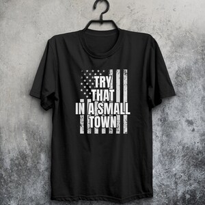 May include: Black t-shirt with a distressed American flag design and the text "TRY THAT IN A SMALL TOWN" in white.