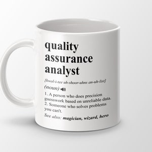Può includere: Una tazza in ceramica bianca con un design nero che recita "quality assurance analyst" e una definizione del termine. La definizione include l'ortografia fonetica della parola e una descrizione divertente del lavoro.
