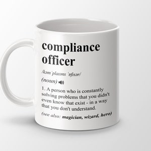 Op de afbeelding: Een witte keramische mok met een zwart ontwerp waarop "compliance officer" staat en de term wordt gedefinieerd als "iemand die voortdurend problemen oplost waarvan je niet eens wist dat ze bestonden - op een manier die je niet begrijpt." De definitie bevat ook "(zie ook: tovenaar, tovenaar, held)".
