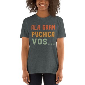 May include: A dark heather grey t-shirt with the text "ALA GRAN PUCHICA VOS..." printed in a retro style with orange, yellow, and green colors.