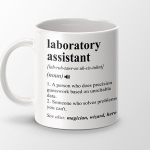 Op de afbeelding: Een witte keramische mok met een zwart ontwerp waarop "laboratory assistant" staat en de term wordt gedefinieerd als "iemand die nauwkeurige schattingen maakt op basis van onbetrouwbare gegevens" en "iemand die problemen oplost die je niet kunt oplossen". Het ontwerp bevat ook de fonetische spelling van het woord en de zin "Zie ook: tovenaar, tovenaar, held".