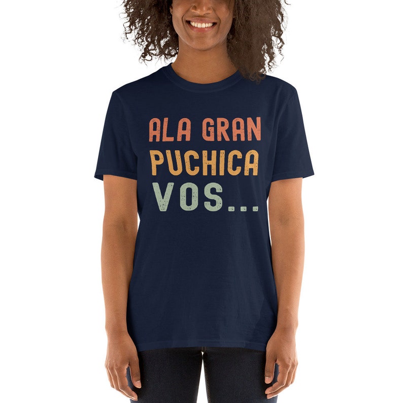 May include: A navy blue t-shirt with the text "ALA GRAN PUCHICA VOS..." in a vintage style font with orange, yellow, and green colors.