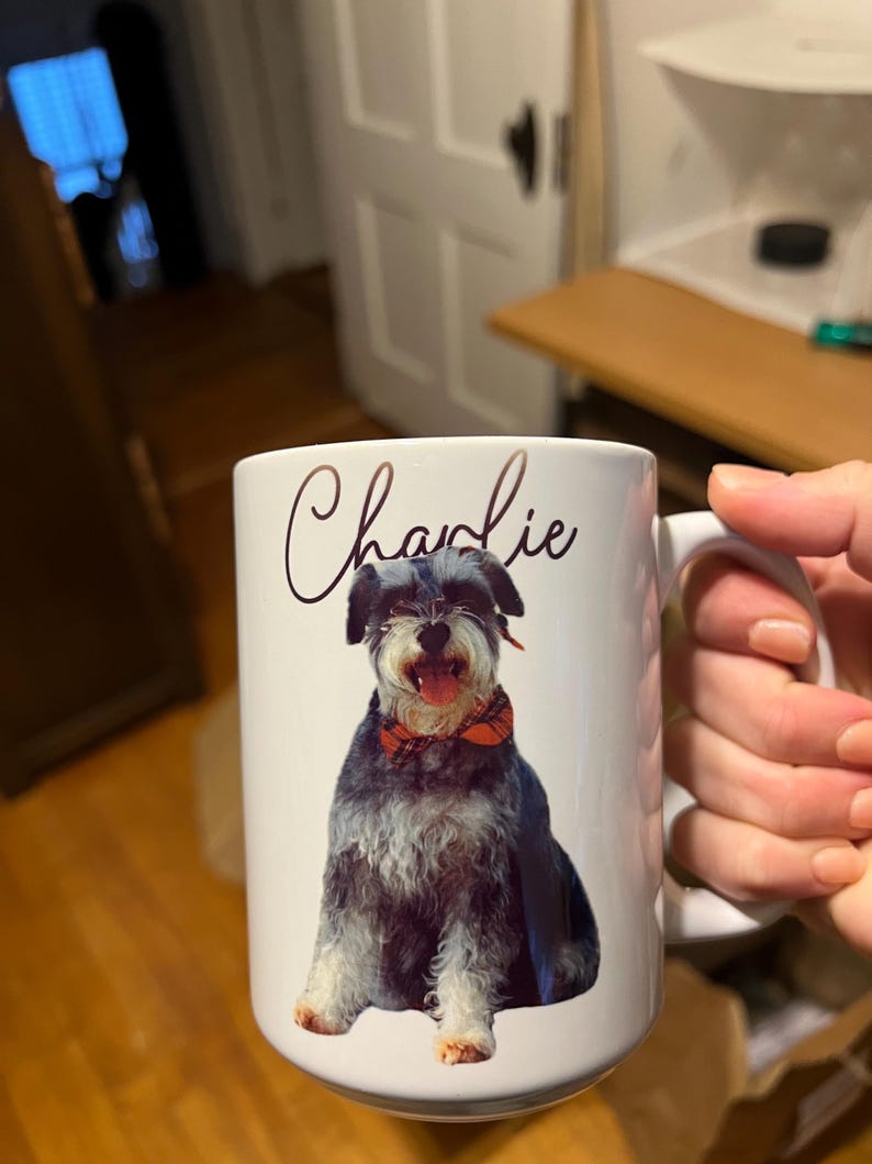 May include: White ceramic mug featuring a black and grey dog wearing a red and black bow tie. The dog's name, "Charlie", is written in cursive on the mug.