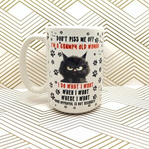 May include: White ceramic mug with a black grumpy cat graphic and the text "DON'T PISS ME OFF I'M A GRUMPY OLD WOMAN I DO WHAT I WANT WHEN I WANT WHERE I WANT YOUR APPROVAL IS NOT REQUIRED". The mug has a large handle.