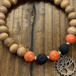 May include: A wooden beaded bracelet with orange and black beads, a silver tree charm, and a silver bead with a red stone.