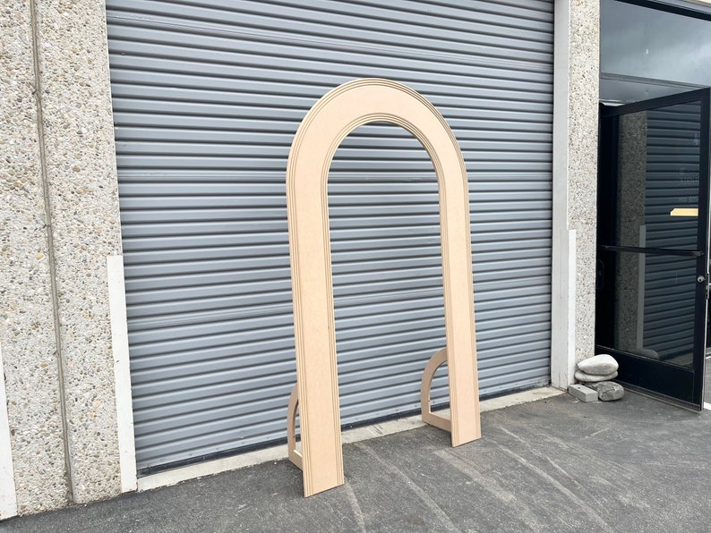 May include: A wooden archway with a rounded top and a natural wood finish. The archway is freestanding and has a simple design.