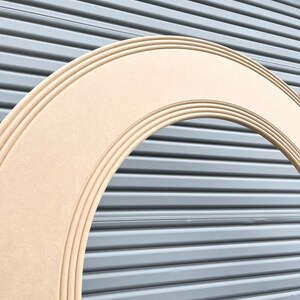 May include: A large, unfinished, wooden archway with a rounded top and multiple layers of molding. The archway is made of light brown wood and is set against a gray background.