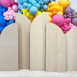 May include: Five arched cardboard backdrops in various sizes, all in a light beige color, with a subtle wood grain texture. The backdrops are arranged in a row, with the largest backdrop in the center and the smallest backdrops on either end.