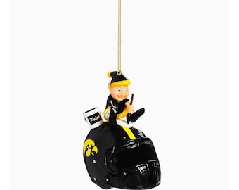 May include: A black and yellow Christmas ornament featuring a cartoon elf painting a black football helmet with the University of Iowa logo. The elf is sitting on the helmet and holding a paintbrush. The paint can says "Paint".