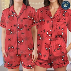 May include: A red pajama set featuring a repeating pattern of Spider-Man masks and black spider webs. The short-sleeved button-down shirt has a notched collar and black piping, paired with matching shorts that have an elasticized waistband.