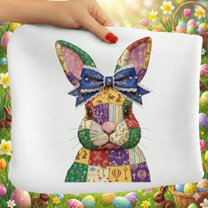 Op de afbeelding: Een wit kussen met een patchwork konijn ontwerp. Het konijn heeft grote oren, een blauwe strik en een roze neus. Het patchwork bevat verschillende patronen en kleuren, perfect voor paasdecoratie.