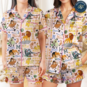 May include: A light pink pajama set featuring a repeating pattern of Lion King characters including Simba, Pumbaa, Timon, Scar, and Rafiki, interspersed with the text Mark and the letter M, finished with pink piping on the collar and shorts.