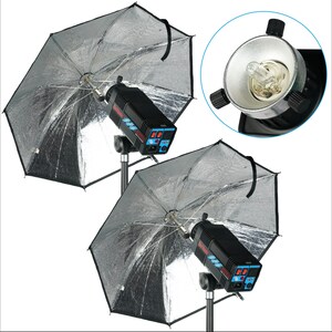 May include: Two silver studio photography umbrellas with black trim and black stands. Each umbrella is attached to a black and blue flash unit with a silver reflector.