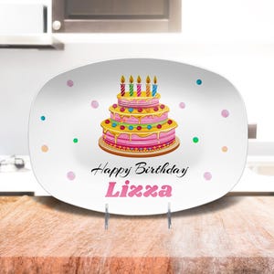 May include: White oval serving platter with a pink and yellow birthday cake with candles and the text "Happy Birthday Lizza".