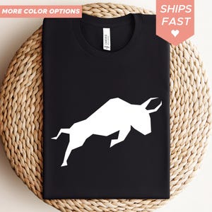 Könnte beinhalten: Schwarzes T-Shirt mit weißem geometrischen Bullenmuster. Das T-Shirt hat einen Rundhalsausschnitt und ein "Canvas"-Etikett. Die Wörter "MORE COLOR OPTIONS" und "SHIPS FAST" sind ebenfalls sichtbar.