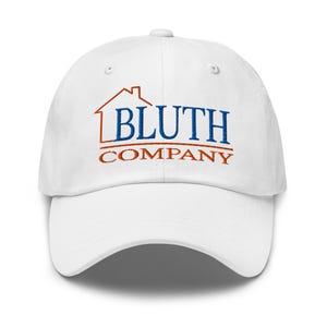 Puede incluir: Gorra de béisbol blanca con un logotipo bordado de una casa con el texto "Bluth Company" en azul y naranja.