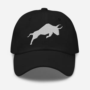 Puede incluir: Una gorra de béisbol negra con una silueta de toro bordada en blanco.