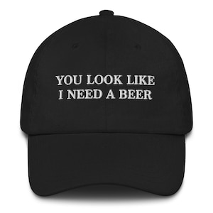 May include: Black baseball cap with white embroidered text that reads "You look like I need a beer."