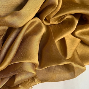 May include: A golden sheer fabric with a smooth, silky texture. The fabric is draped and folded, showcasing its flowing nature.