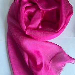 Peut inclure: Écharpe fuchsia vif, drapée et pliée, mettant en valeur un tissu doux et fluide. L'écharpe a un éclat subtil et un bord effiloché. La couleur rose vif est uniforme sur tout le textile.