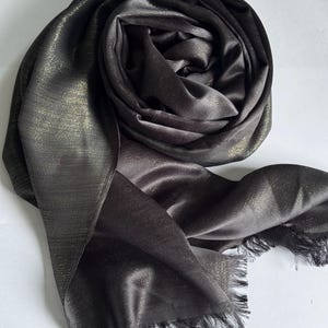 May include: A black and gold shimmer scarf with a fringed edge. The scarf is made of a soft, silky material.