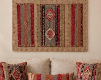 May include: A rectangular wall hanging featuring three vertical woven fabric panels with red, orange, and gray stripes and diamond patterns, mounted on a tan burlap backing. Below, three matching rectangular throw pillows are displayed.