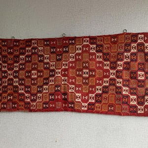 K&ouml;nnte beinhalten: Ein roter, orangefarbener und wei&szlig;er Teppich mit geometrischem Muster. Der Teppich ist mit komplizierten Details gewebt und hat ein traditionelles Aussehen.
