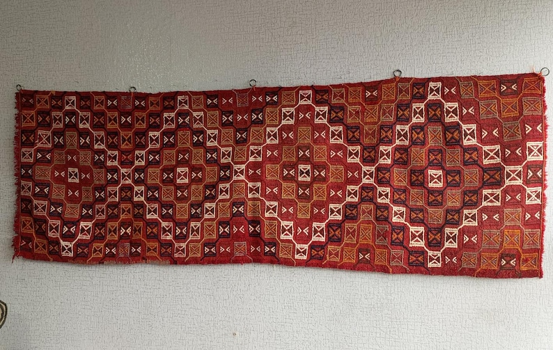 K&ouml;nnte beinhalten: Ein roter, orangefarbener und wei&szlig;er Teppich mit geometrischem Muster. Der Teppich ist mit komplizierten Details gewebt und hat ein traditionelles Aussehen.