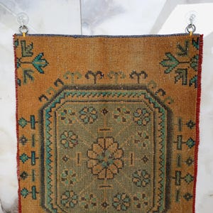 Pu&ograve; includere: Un tappeto rettangolare vintage con un design a medaglione centrale. Il tappeto presenta un campo marrone dorato caldo con un motivo geometrico centrale verde e oro. Accenti turchese e rossi incorniciano il design, creando un'estetica rustica e invecchiata.