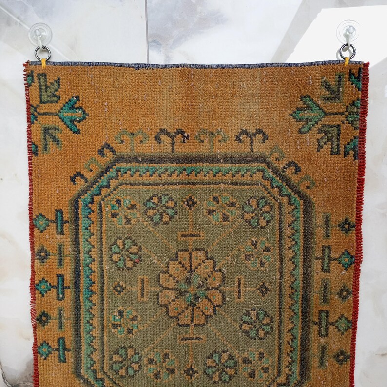 Pu&ograve; includere: Un tappeto rettangolare vintage con un design a medaglione centrale. Il tappeto presenta un campo marrone dorato caldo con un motivo geometrico centrale verde e oro. Accenti turchese e rossi incorniciano il design, creando un'estetica rustica e invecchiata.
