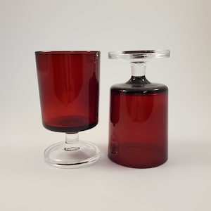 Puede incluir: Dos vasos para beber de vidrio rojo, uno con un tallo y una base de vidrio transparente, el otro con una parte superior y una base de vidrio transparente.