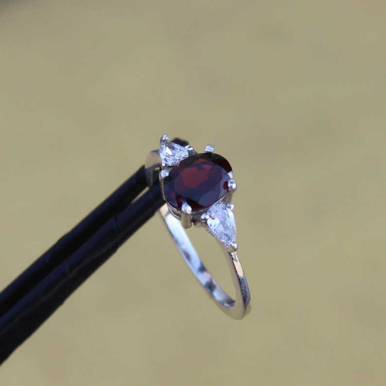 May include: A silver ring with a red oval gemstone and two smaller pear-shaped clear gemstones.