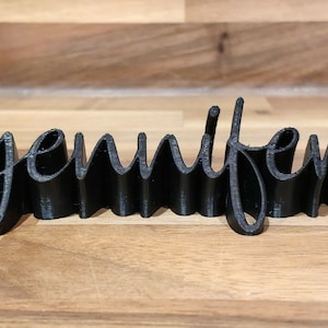 May include: A black 3D printed word sign that reads "jennifer".