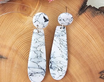May include: A pair of dangle earrings with a white and black marbled design. The earrings have a round top and a teardrop-shaped bottom.