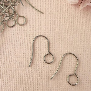 May include: Two silver earring hooks on a pink textured surface. The hooks are made of metal and have a loop at the top and a hook at the bottom.
