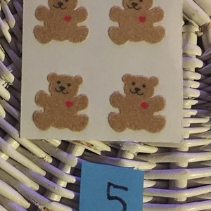 May include: Four brown teddy bear stickers with red hearts on a white background. The stickers are arranged in a 2x2 grid. The number 5 is written on a blue sticky note.