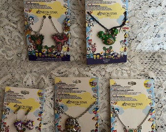 May include: Five Neon Star by tokidoki jewelry sets on cardboard backing cards. Includes two magnetic friendship necklaces, a cactus pendant necklace, owl earrings, a heart-shaped pendant necklace, and a Love pendant necklace with a cactus charm.